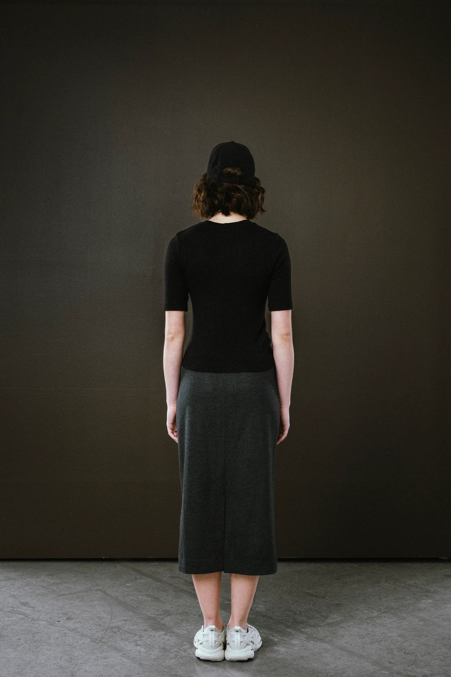 Person wearing a black top and dark skirt against a dark background