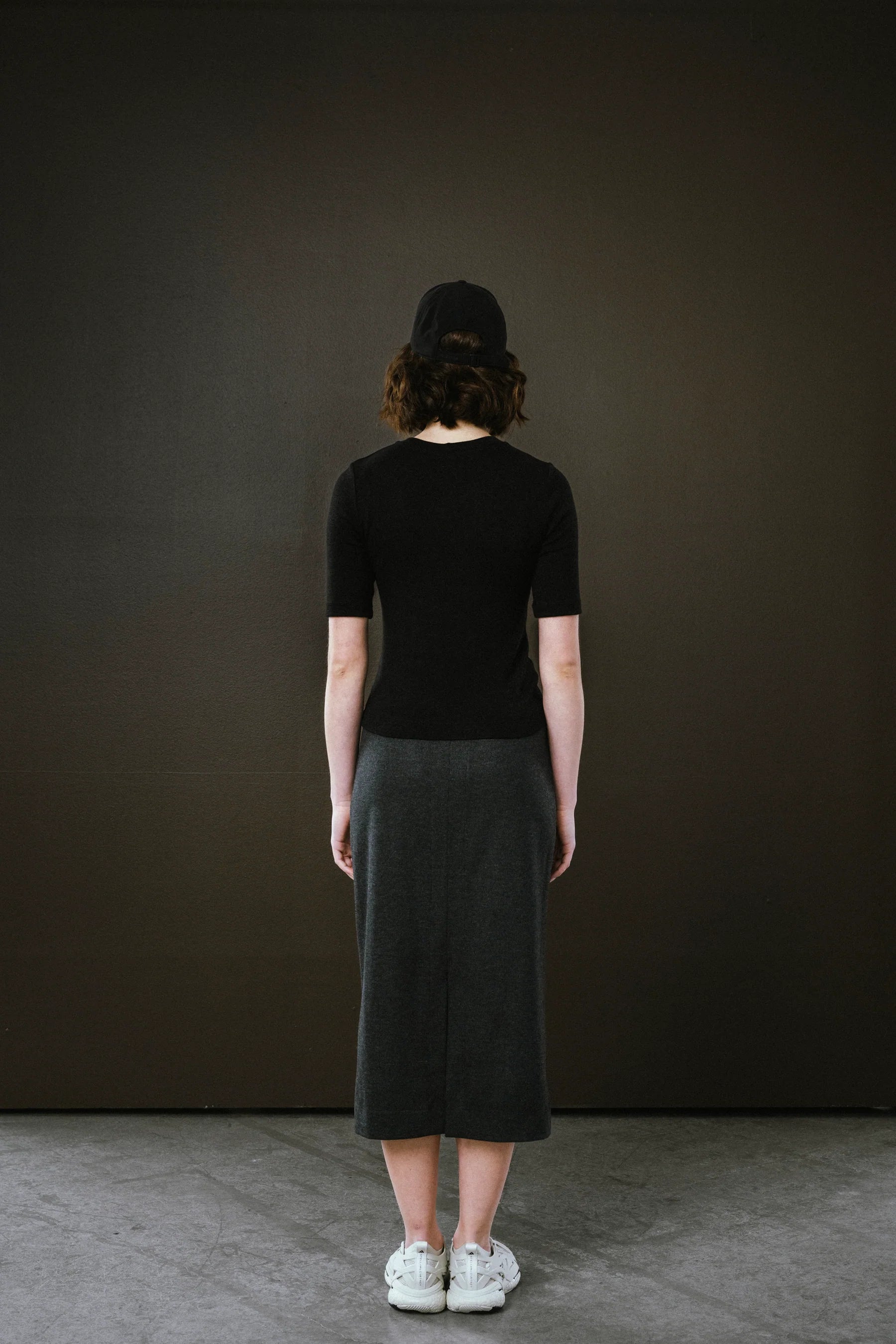 Person wearing a black top and dark skirt against a dark background