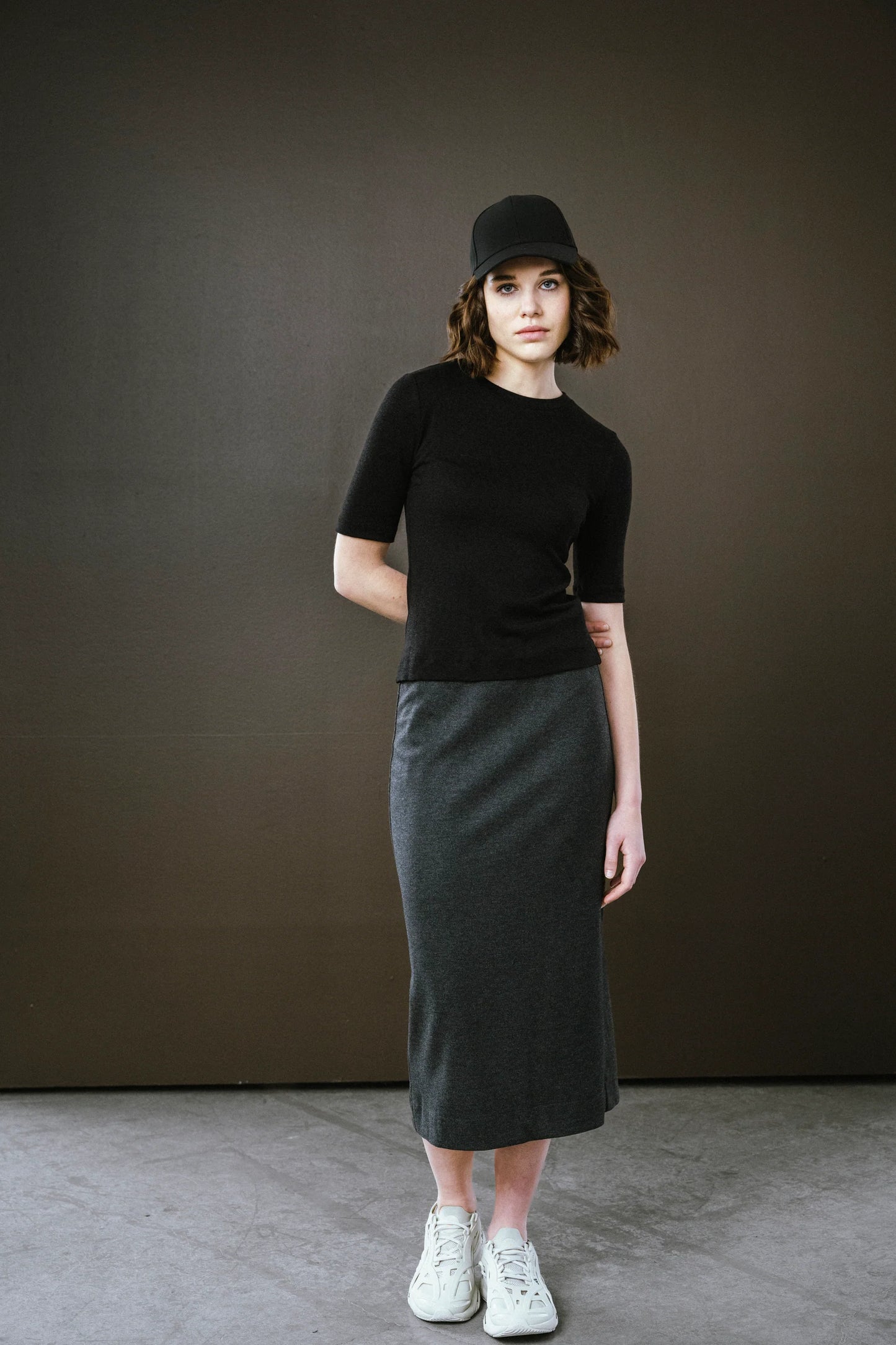 Woman wearing a black top and gray skirt against a dark background