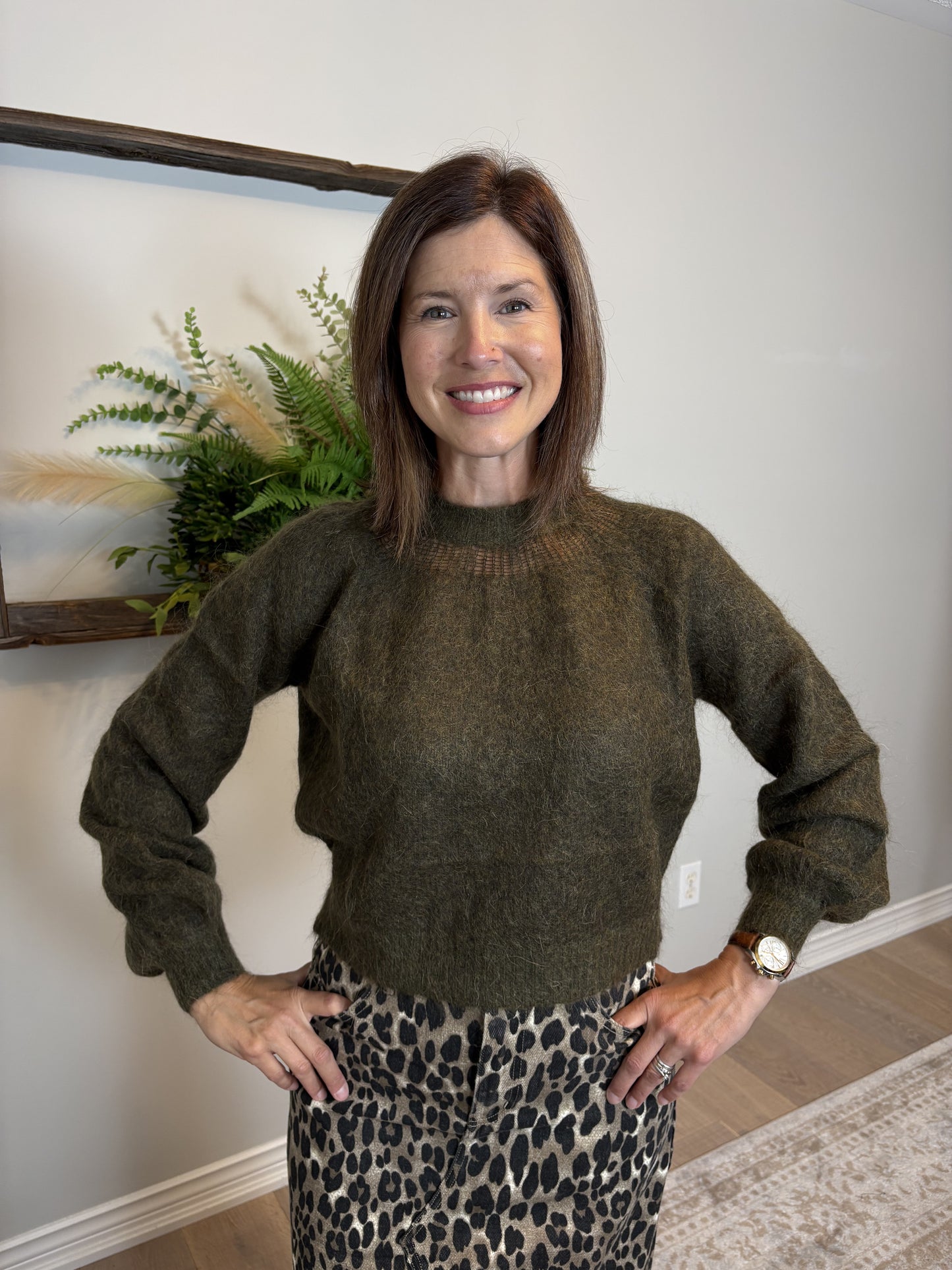 Woman wearing a green sweater and leopard print skirt indoors.