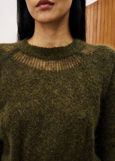 Person wearing a textured green sweater with a blurred background