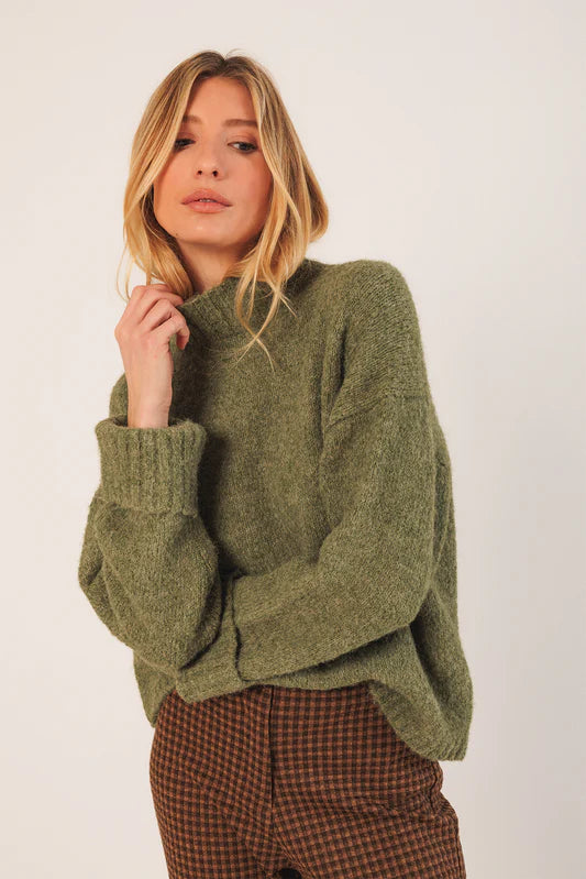 Woman wearing a green sweater and plaid pants against a white background
