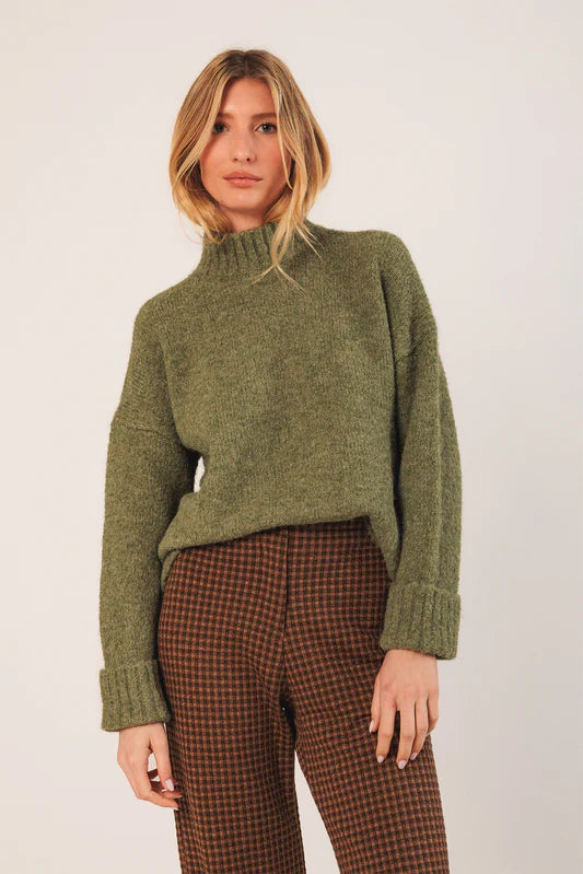 Woman wearing a green sweater and plaid pants against a white background