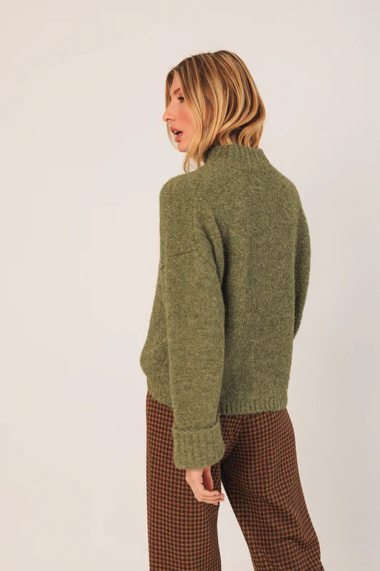 Woman wearing a green sweater and brown checkered pants against a white background