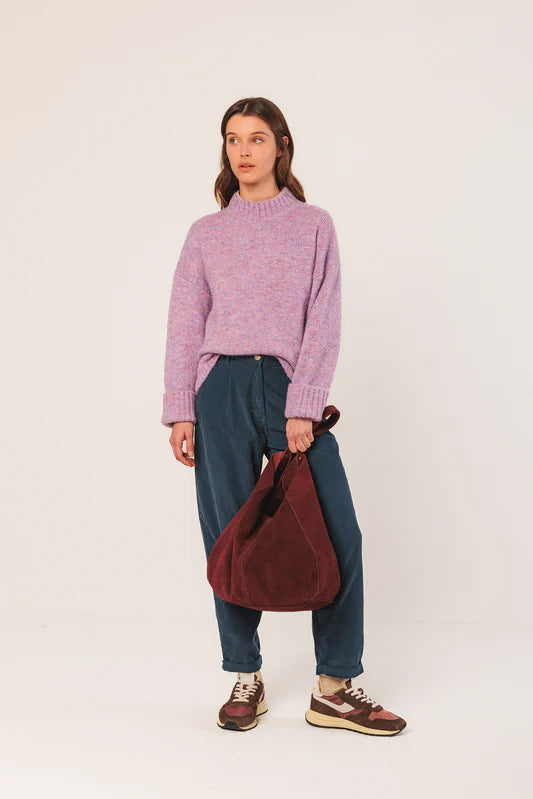 Person wearing a pink sweater, blue pants, and brown shoes holding a red bag on a white background