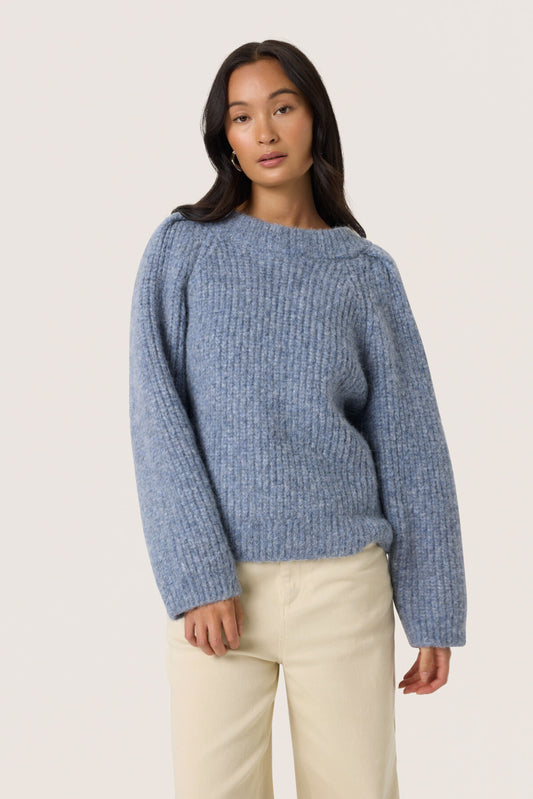 Woman wearing a blue sweater and beige pants on a white background