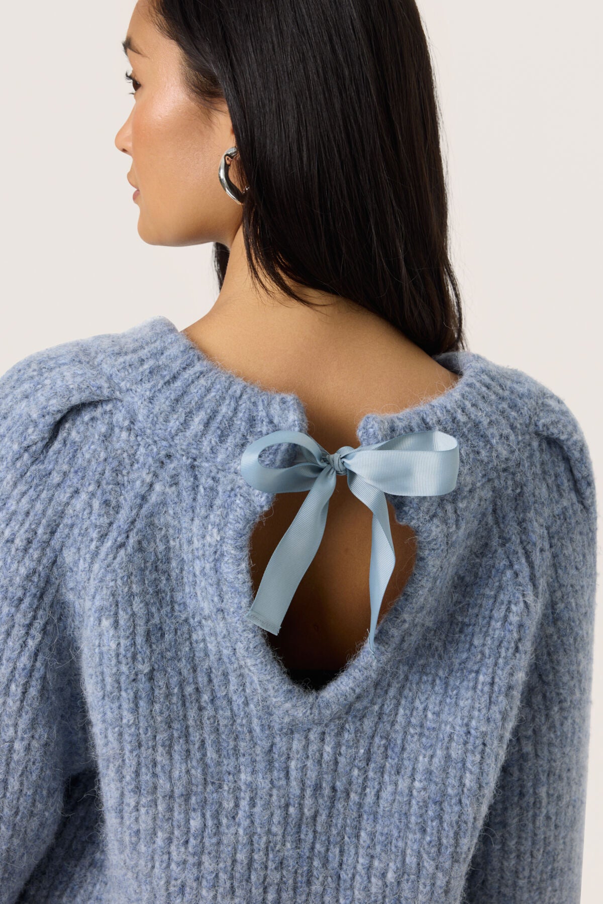 Light blue sweater with a ribbon detail on a plain background