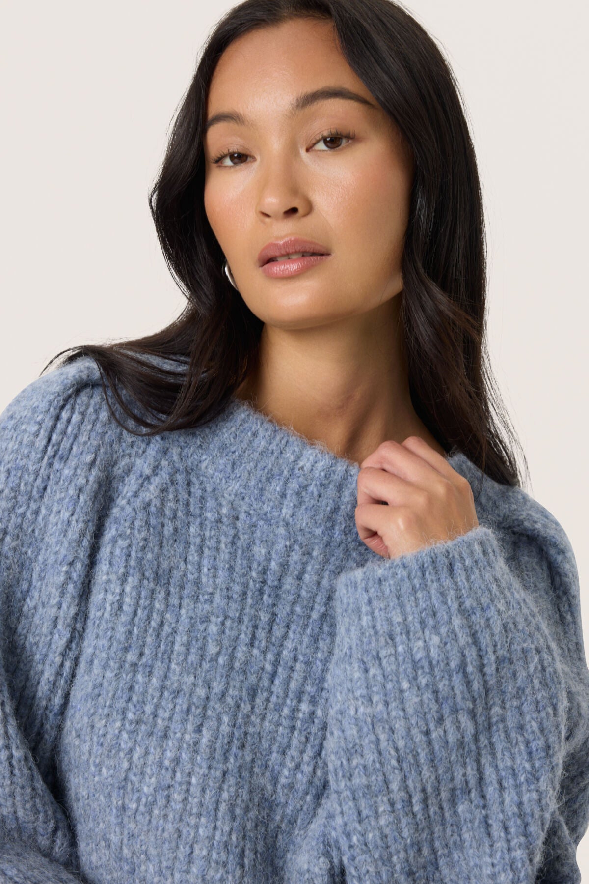 Woman wearing a blue knitted sweater against a plain background