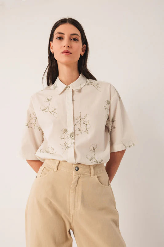 Woman wearing a beige floral blouse and beige pants against a white background