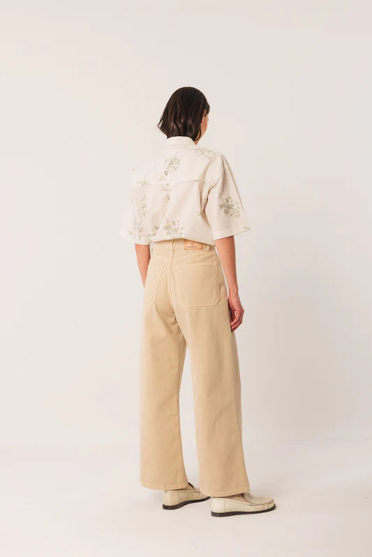 Person wearing a white floral blouse and beige pants on a white background