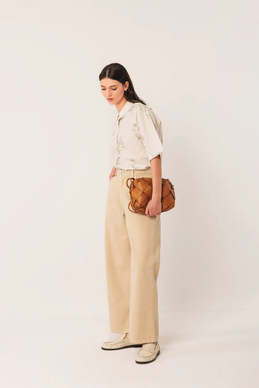 Woman wearing a beige shirt and pants with a brown bag against a white background