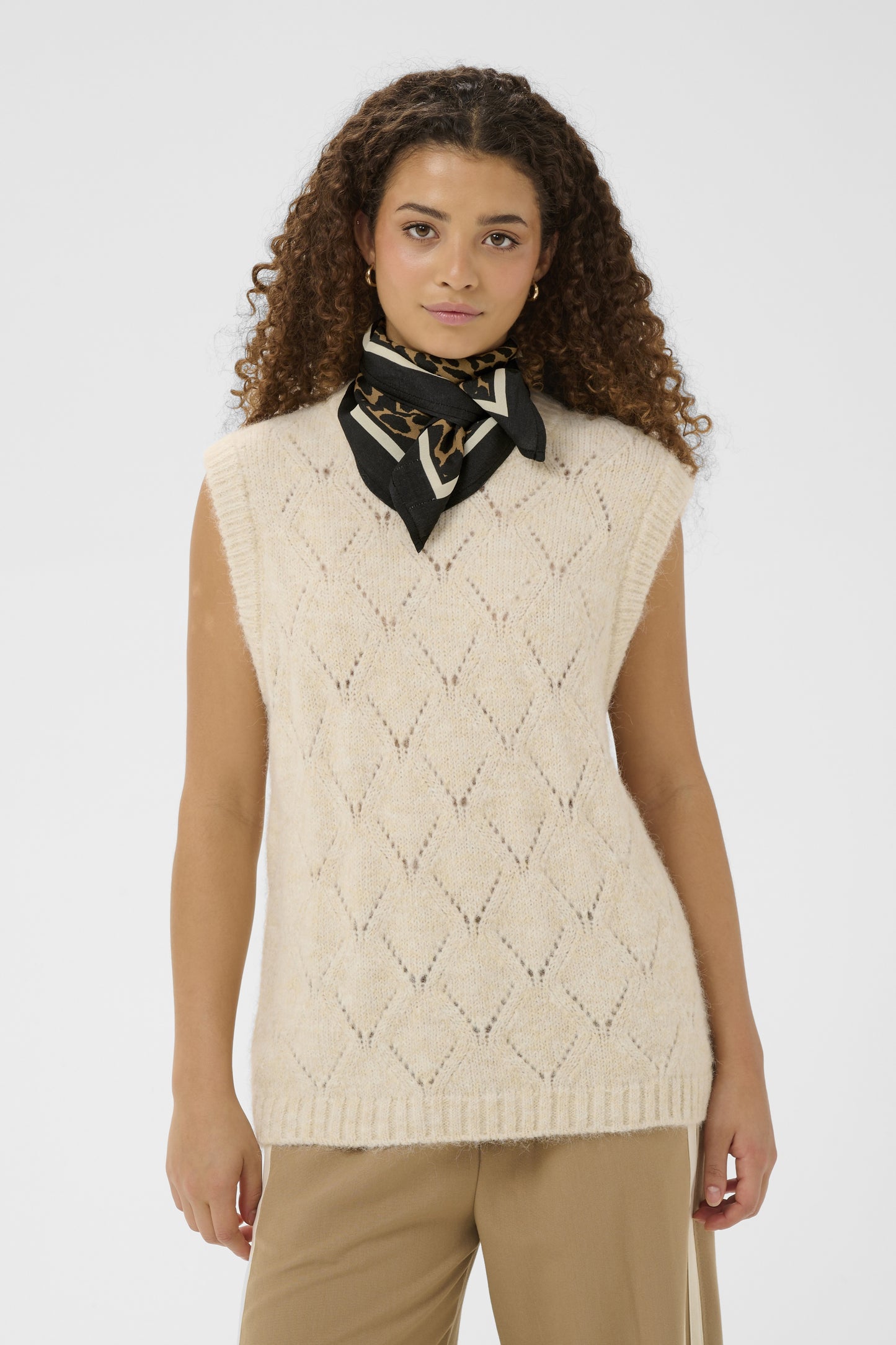 Woman wearing a beige knitted vest with a patterned scarf on a white background