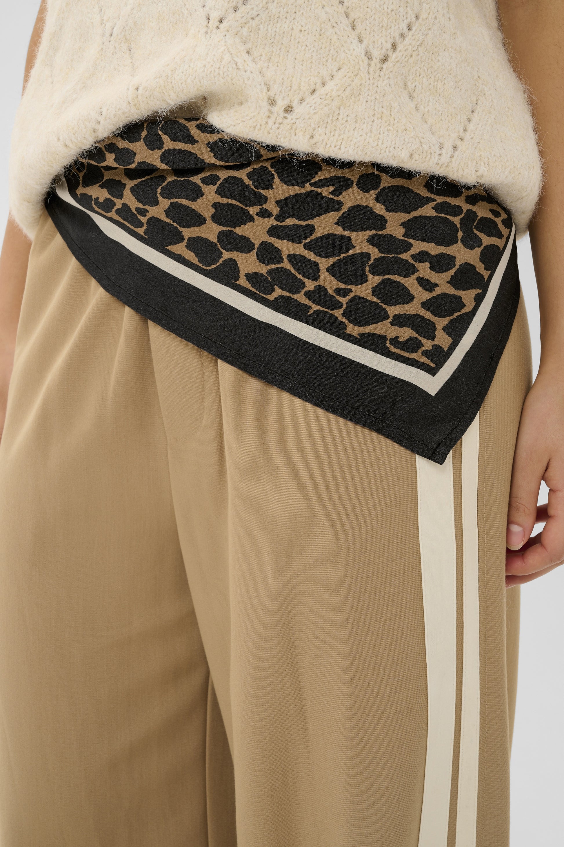 Person wearing a leopard print scarf over a white sweater and beige pants on a plain background