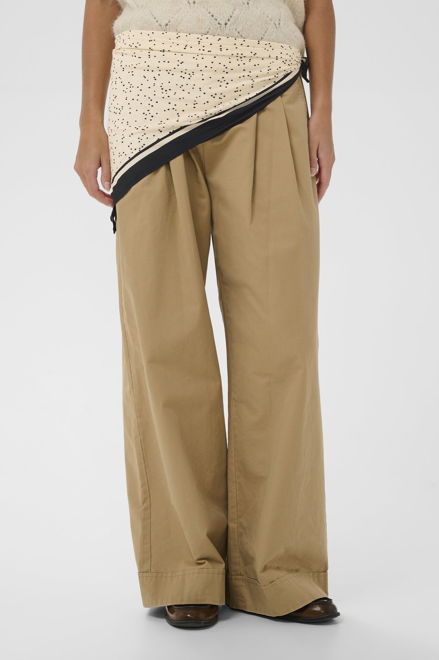 Person wearing beige wide-leg pants with a patterned top on a white background