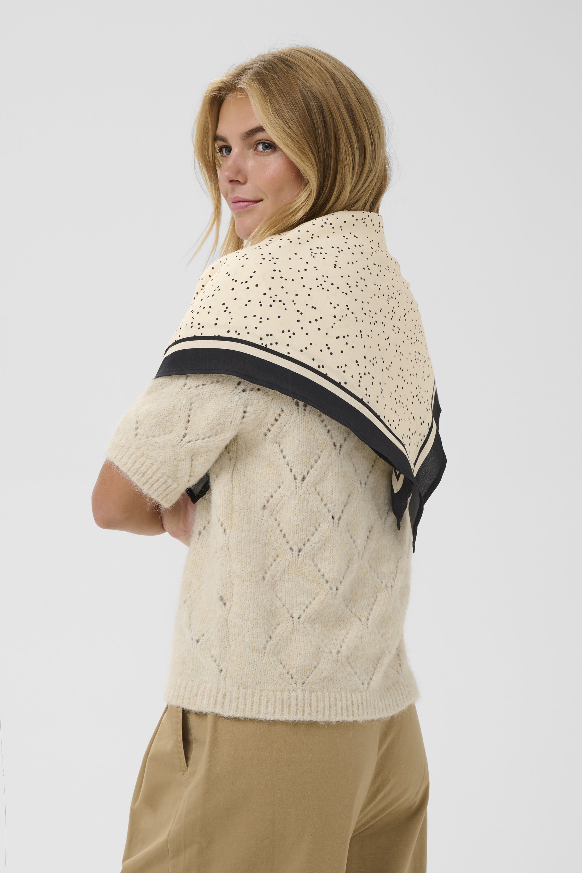 Woman wearing a cream-colored knitted sweater with a black stripe on a white background