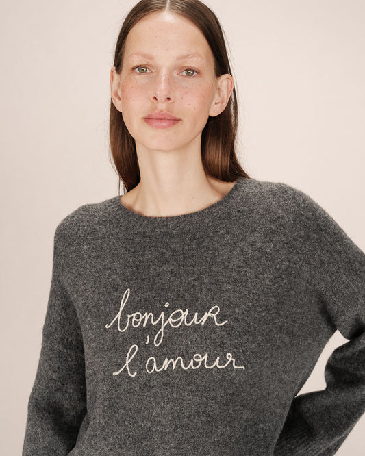 Woman wearing a gray sweater with 'bonjour l'amour' text on a beige background