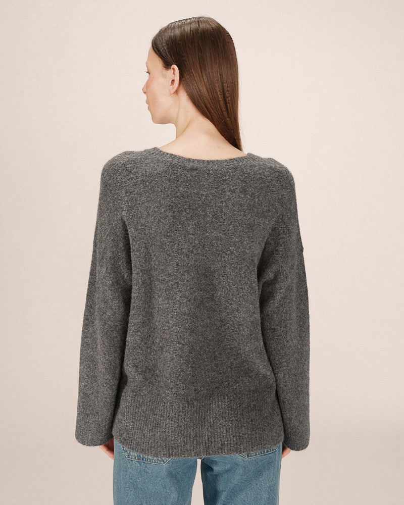 Person wearing a gray sweater against a beige background