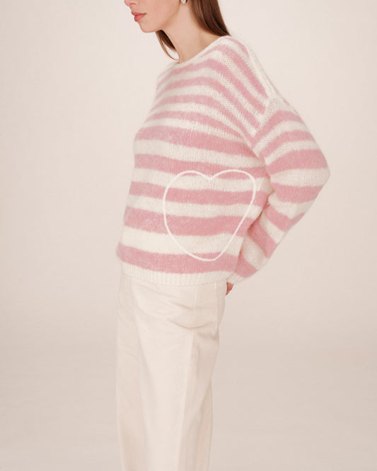 Person wearing a pink and white striped sweater with a heart design on a plain background
