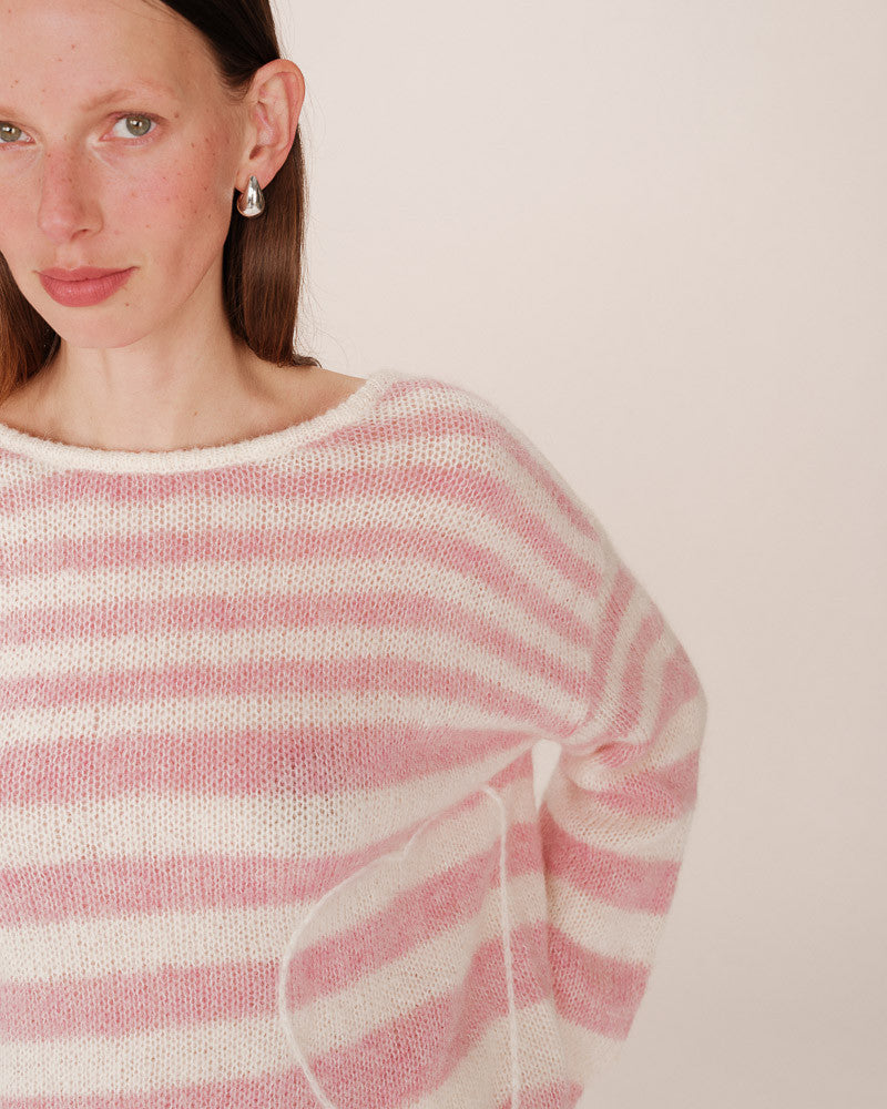 Woman wearing a pink and white striped sweater against a plain background