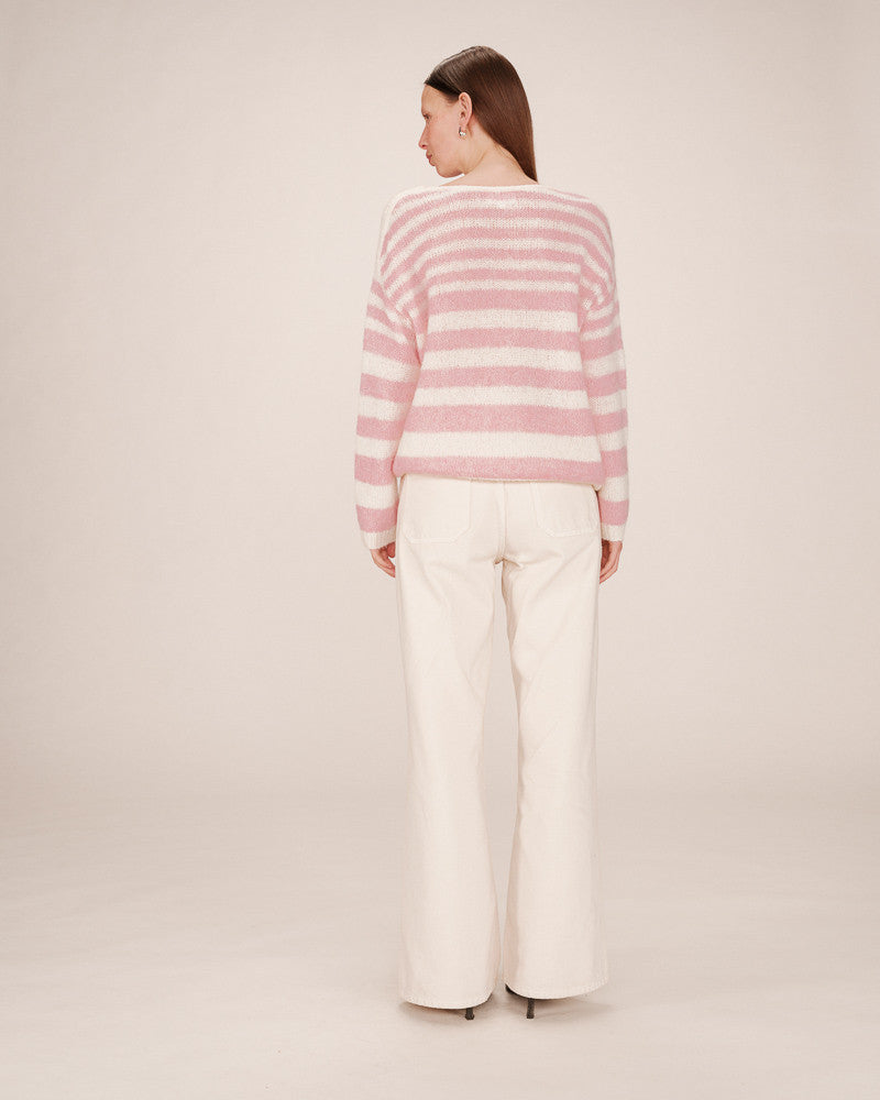 Person wearing a pink and white striped sweater and white pants on a plain background