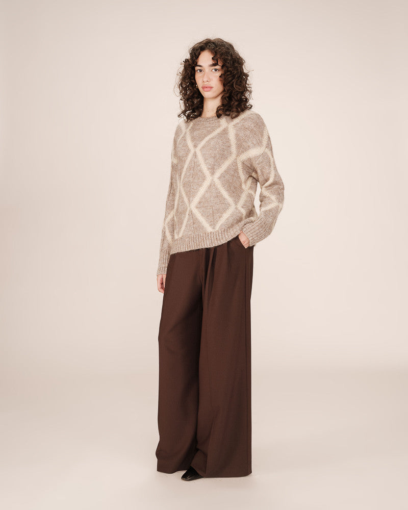 Woman wearing a patterned sweater and brown pants on a plain background