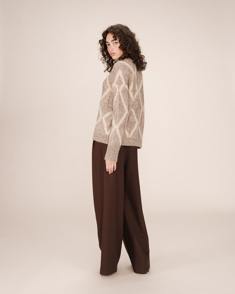 Woman wearing a patterned sweater and brown pants on a plain background