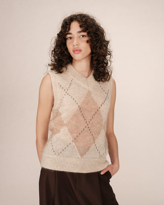 Woman wearing a beige knitted vest with a diamond pattern against a plain background