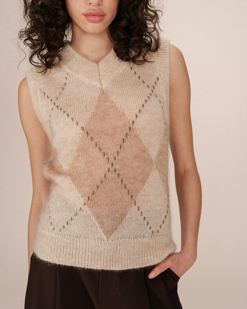 Woman wearing a beige sleeveless knitted vest with a diamond pattern on a plain background