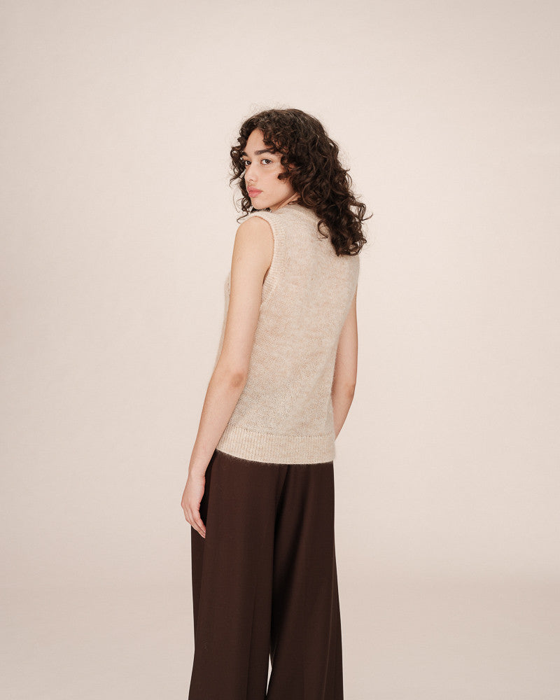 Woman wearing a beige sleeveless top and brown pants on a plain background