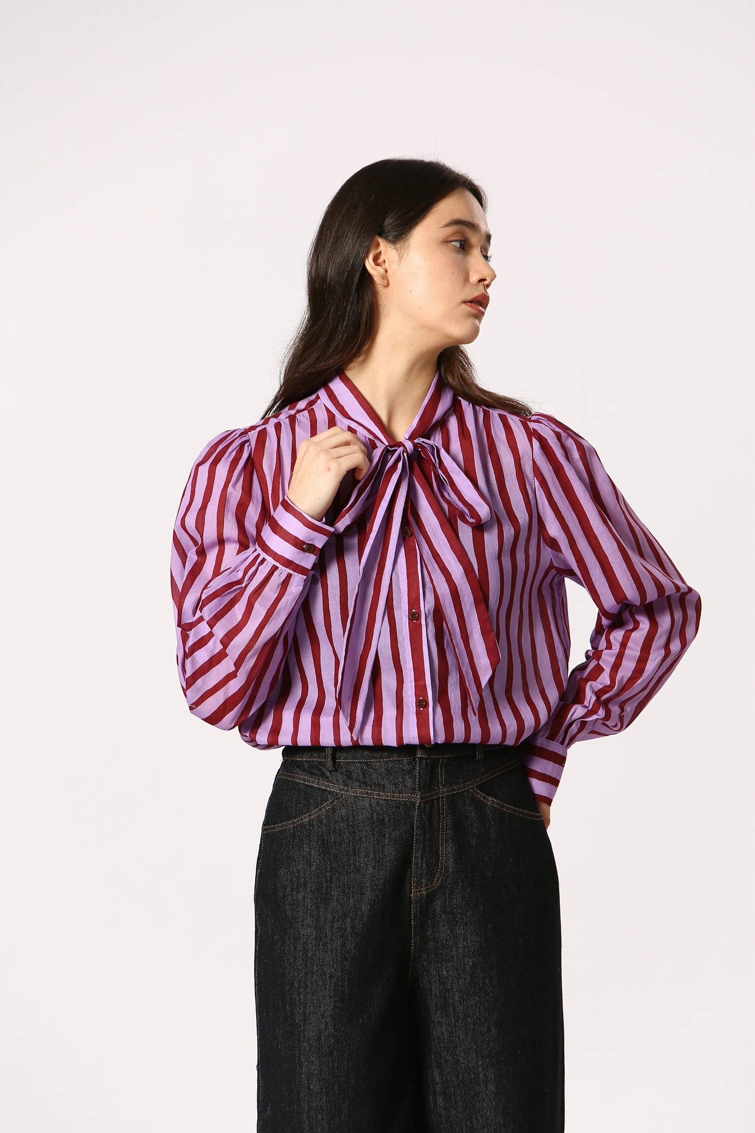 Woman wearing a purple and maroon striped shirt with a bow tie on a white background
