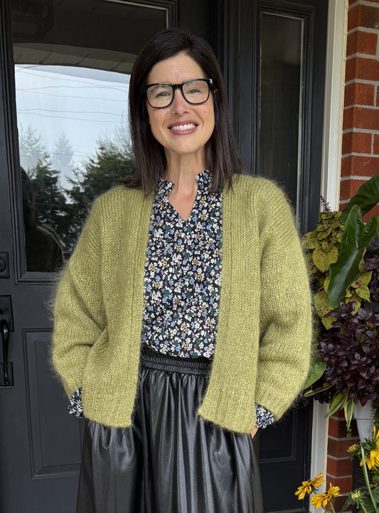 Woman wearing a green cardigan standing in front of a door with flowers in the background