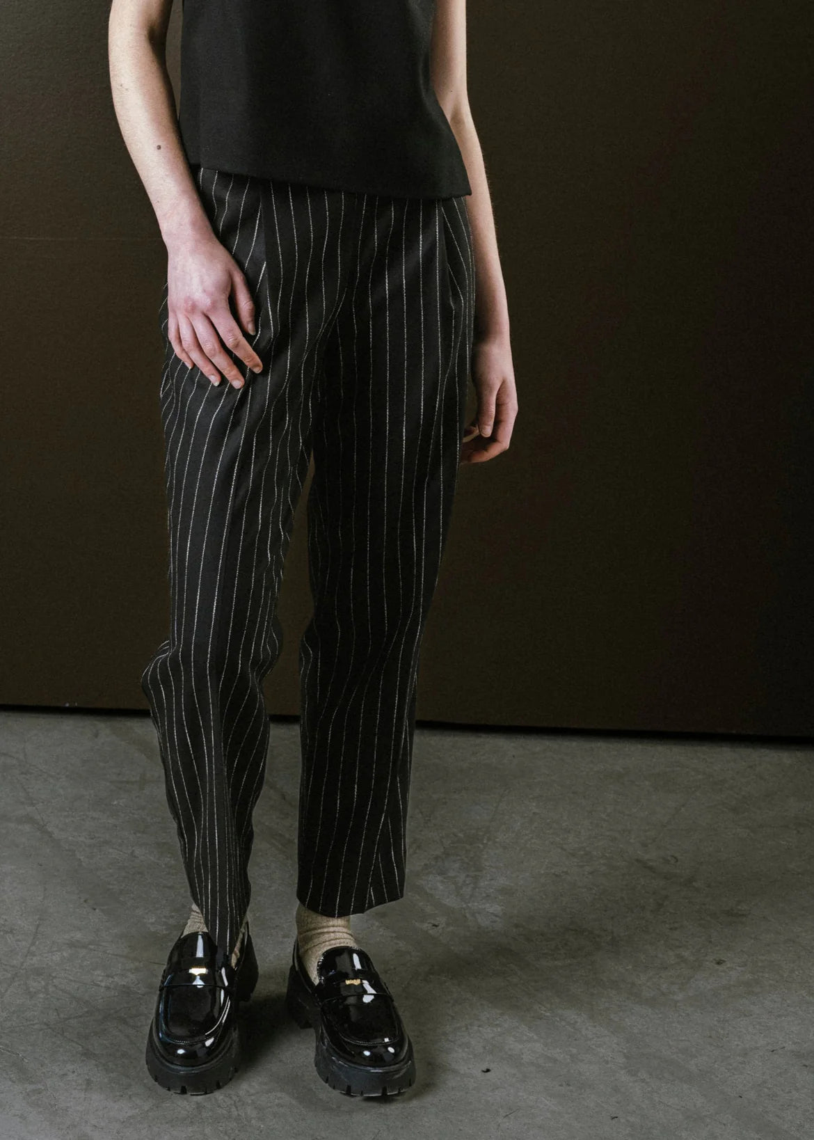 Person wearing black pinstripe pants and black shoes against a brown background
