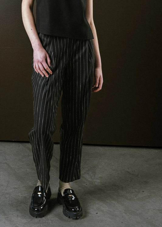 Person wearing black pinstripe pants and black shoes against a brown background