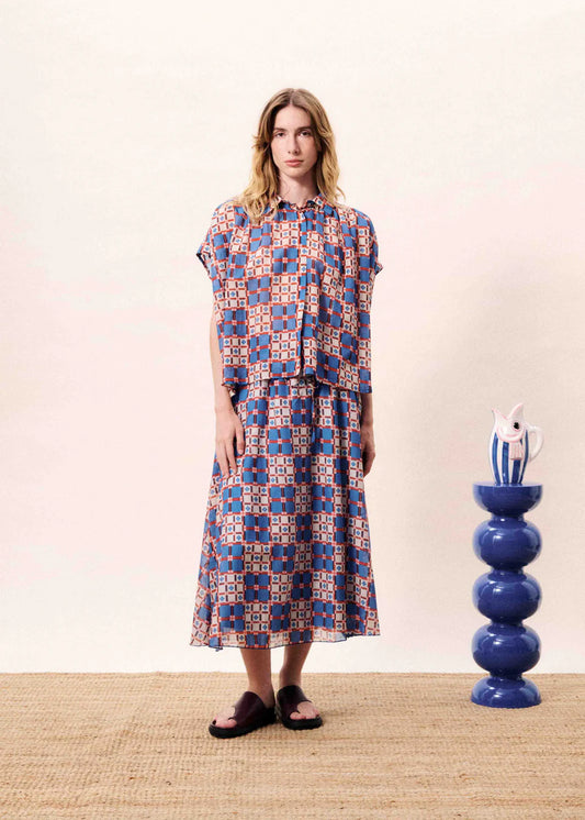 Woman wearing a patterned dress standing next to a blue vase on a beige surface.