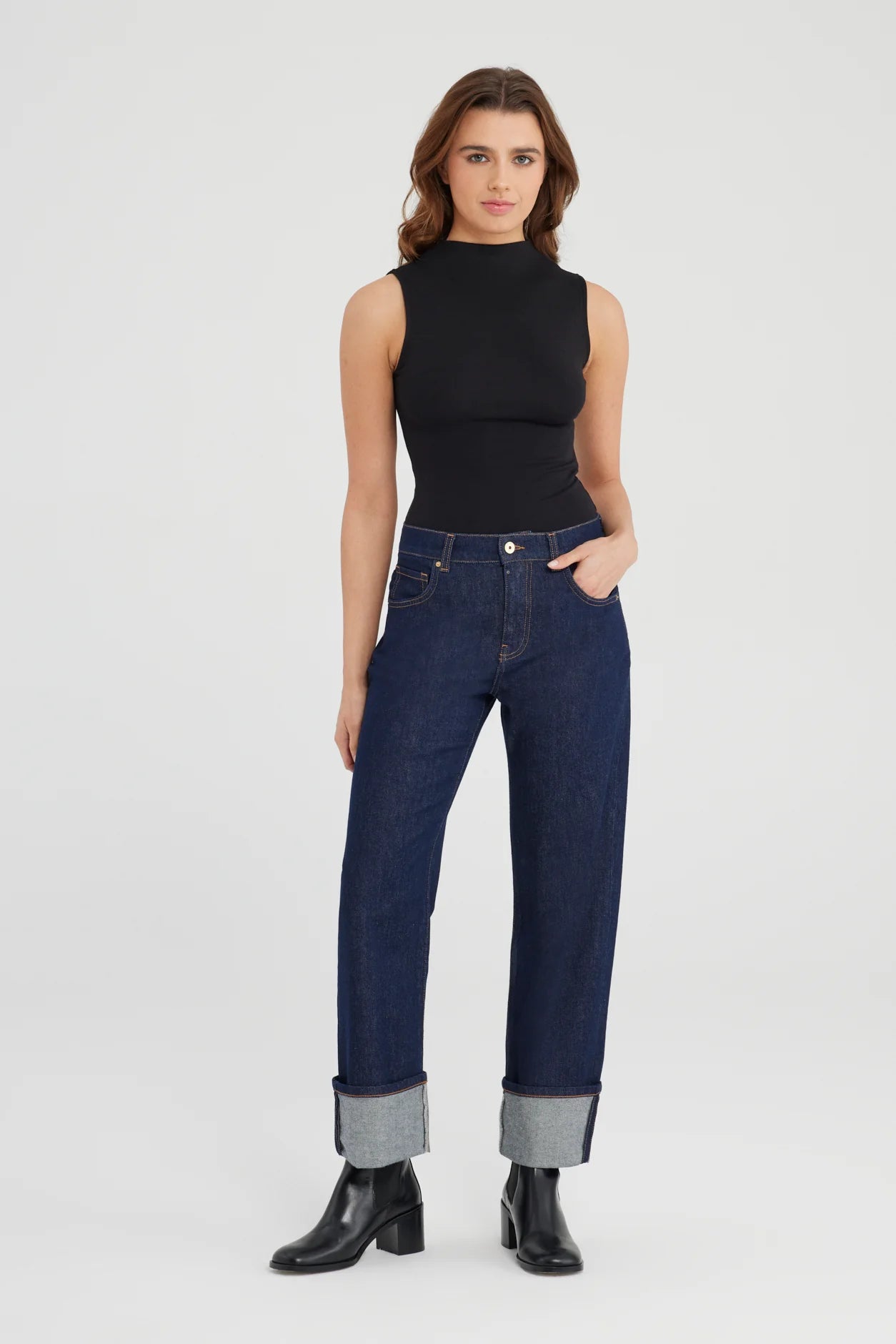 Woman wearing a black sleeveless top and blue jeans on a white background