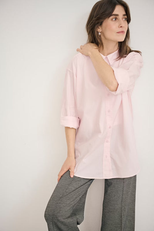 Woman wearing a light pink shirt and gray pants against a plain background
