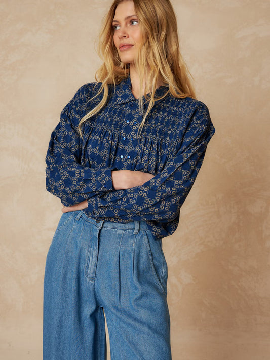 Get ready to turn some heads in our Smoke Detail Blouse by Indi & Cold! Made with soft woven viscose in a beautiful denim blue colour, this blouse features a unique beige geometric pattern and a flattering double button-down front. The rouched detailing across the chest and back adds a touch of fun and playfulness to your outfit. Easy to dress up or down, this is a must-have addition to your wardrobe!