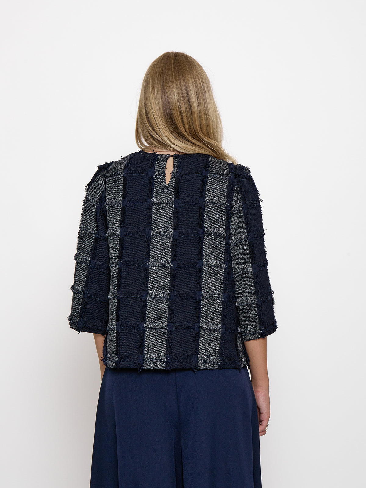 A woman viewed from the back wearing a cropped textured jacket with vertical stripes of navy and gray bouclé-like fabric, paired with navy wide-leg pants, against a plain white background.
