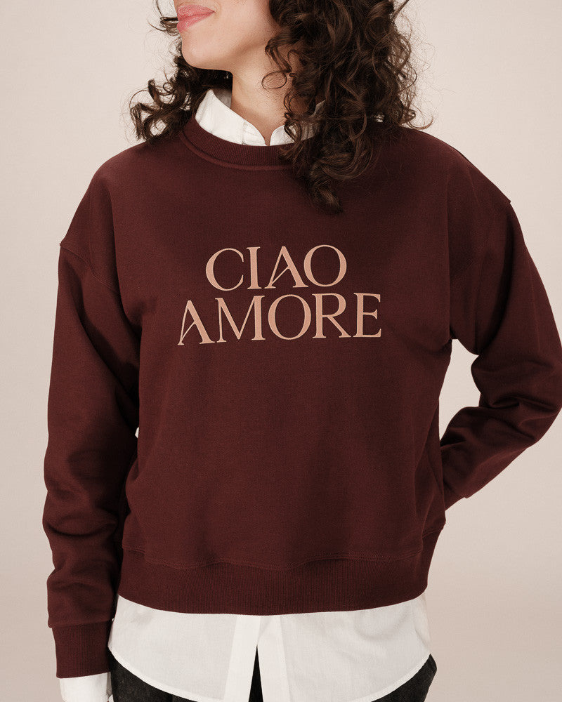Brown sweatshirt with 'CIAO AMORE' text worn by a person on a beige background