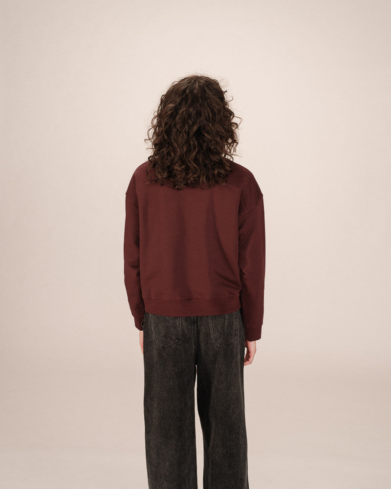 Person wearing a maroon sweater and dark pants against a beige background