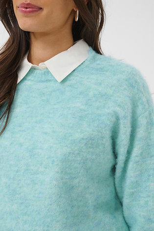 A close-up of a person wearing a fuzzy light aqua sweater over a white collared shirt, with dark hair and part of the face visible against a plain light background.