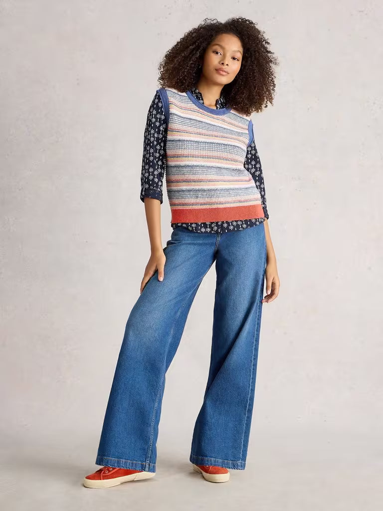 Woman wearing a colorful striped sweater and blue jeans on a plain background