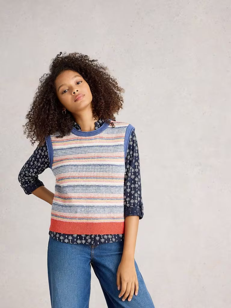 Woman wearing a colorful striped sweater with floral patterns on a plain background