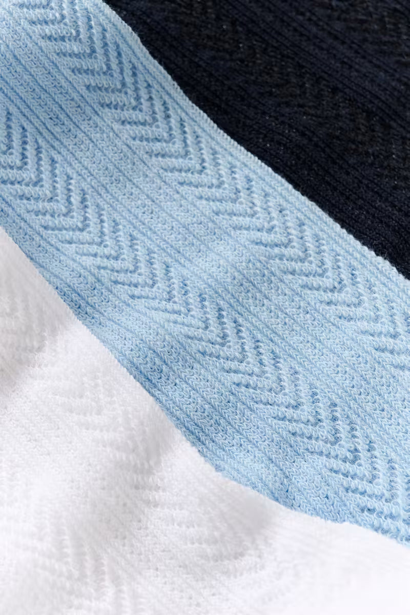 Close-up of a textured knit fabric with a wide light blue chevron-patterned band over white and dark navy sections.