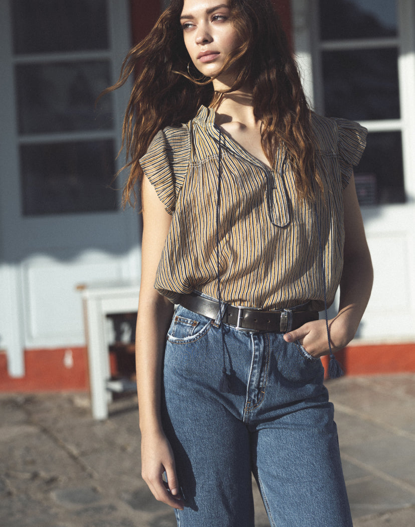 Elevate your wardrobe with the effortless chic of Parisian style with our Sleeveless Striped Blouse by The Korner. Crafted with a flowy sleeve detail and a charming tie v-neck, this blouse exudes sophistication and versatility. Featuring a timeless combination of navy, ochre, and cream thin stripes, it adds a touch of classic elegance to any ensemble. Embrace French-inspired fashion and elevate your look with this must-have piece from The Korner.