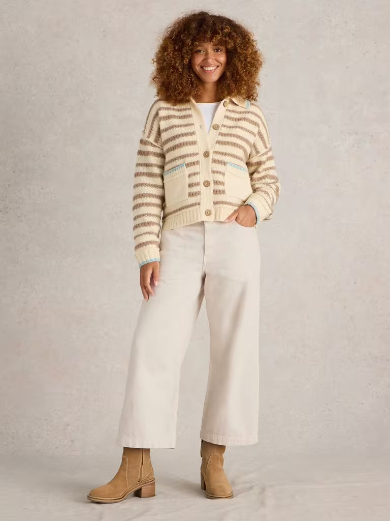 Woman wearing a striped cardigan, white pants, and brown boots on a plain background