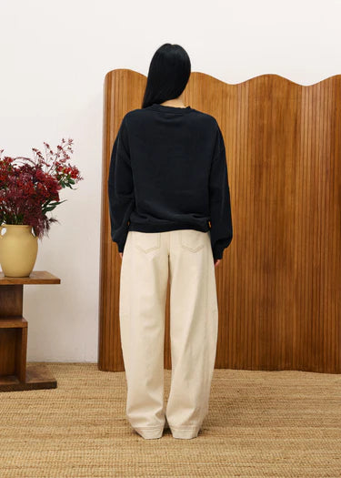 Person wearing a black sweater and beige pants standing in front of a wooden screen.