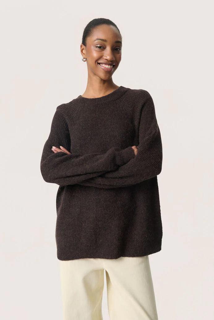 Woman wearing a dark brown sweater with arms crossed against a light background