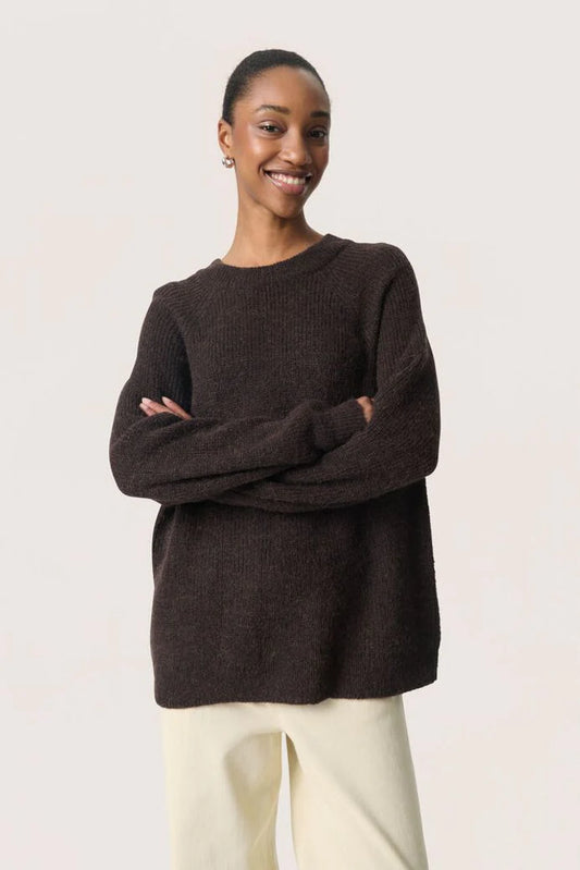 Woman wearing a dark brown sweater with arms crossed against a light background