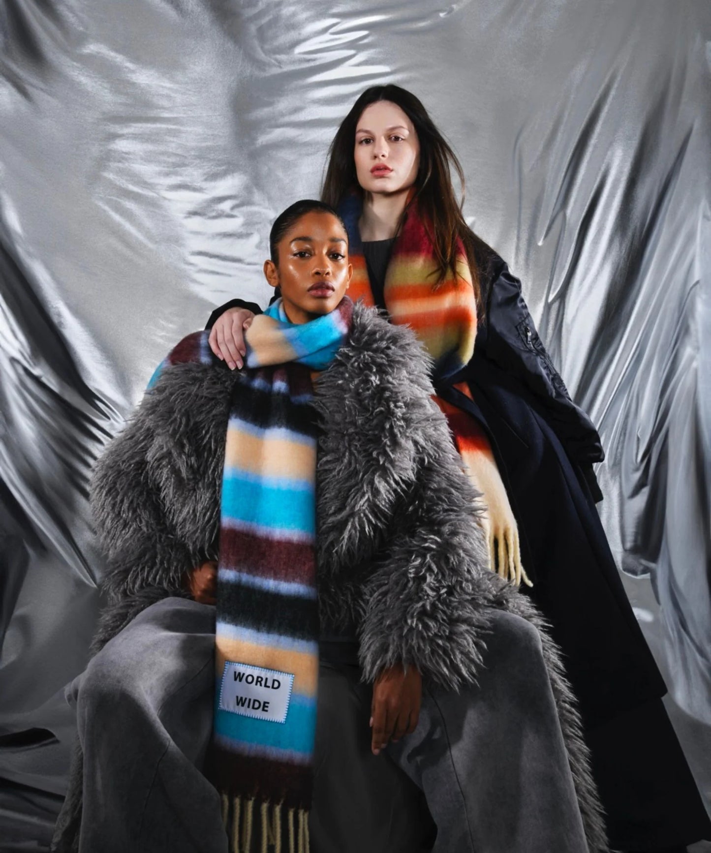 Two people wearing colorful scarves against a textured gray background